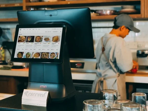 Digital ordering system in a restaurant kitchen with a touchscreen display and a chef at work.