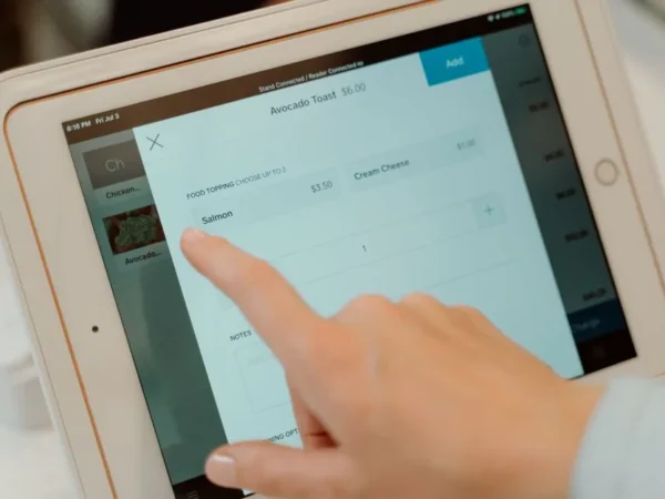 Close-up of a person's finger interacting with a point of sale tablet screen.