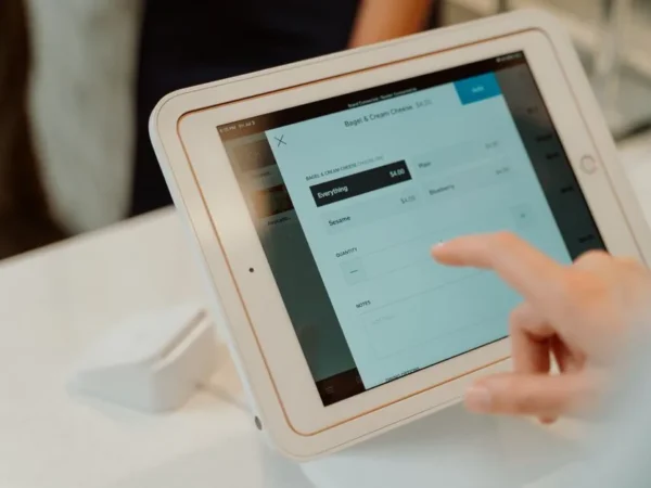 A person uses a tablet-based point-of-sale system by selecting options on a touchscreen device.