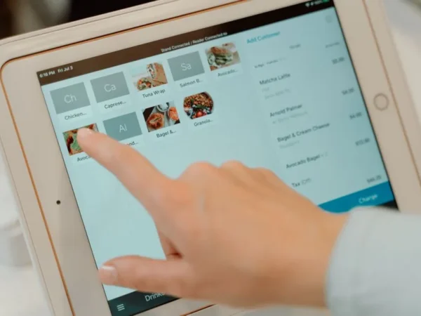 Finger tapping on a tablet screen to select food items in a restaurant setting.