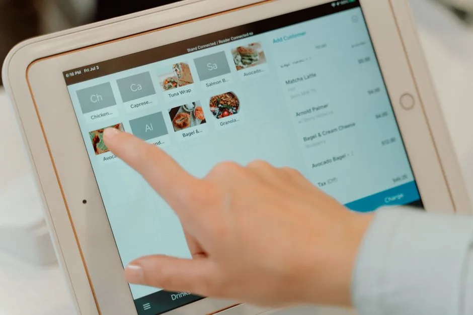 Finger tapping on a tablet screen to select food items in a restaurant setting.